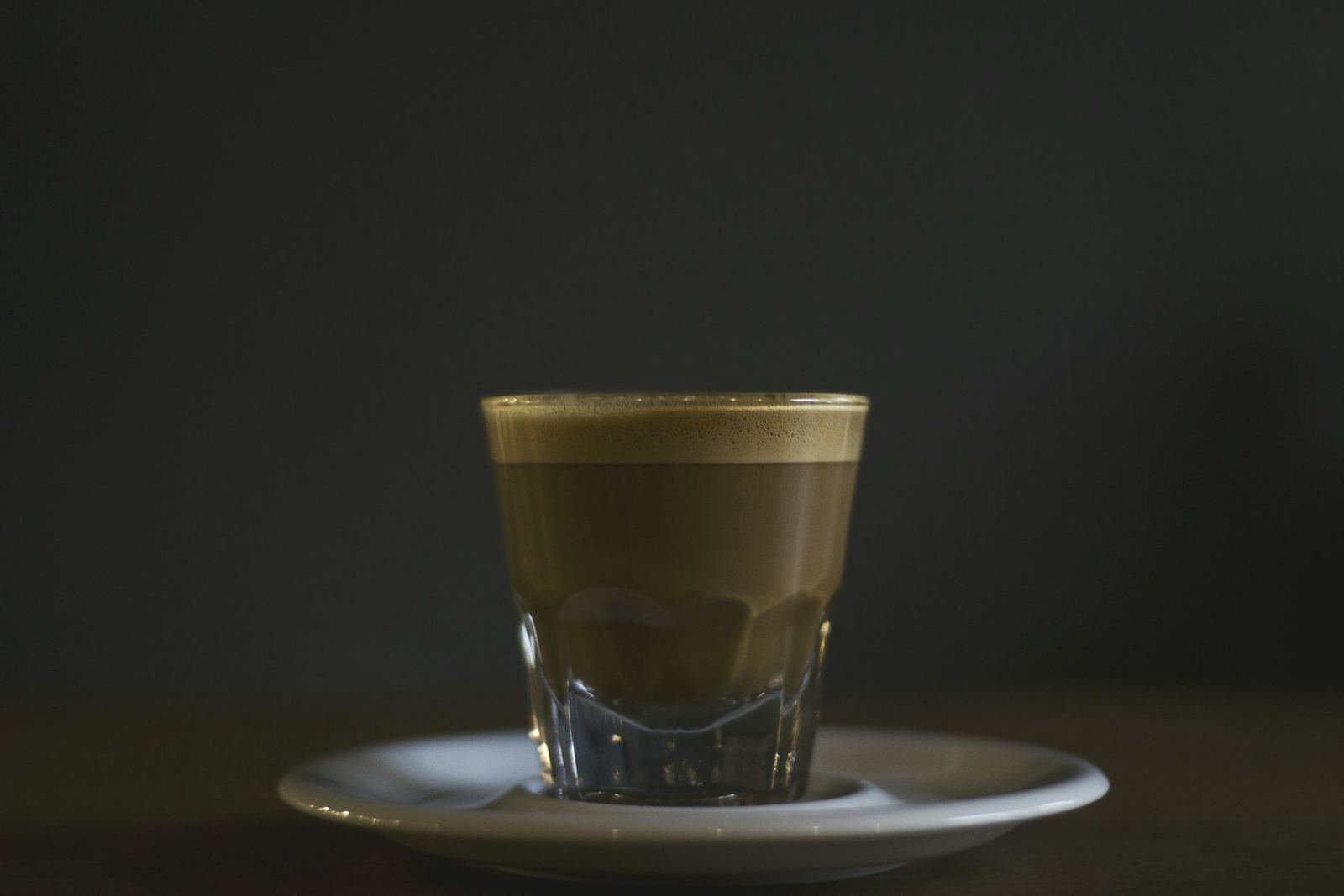 Coffee in a glass on a saucer, against a dark background