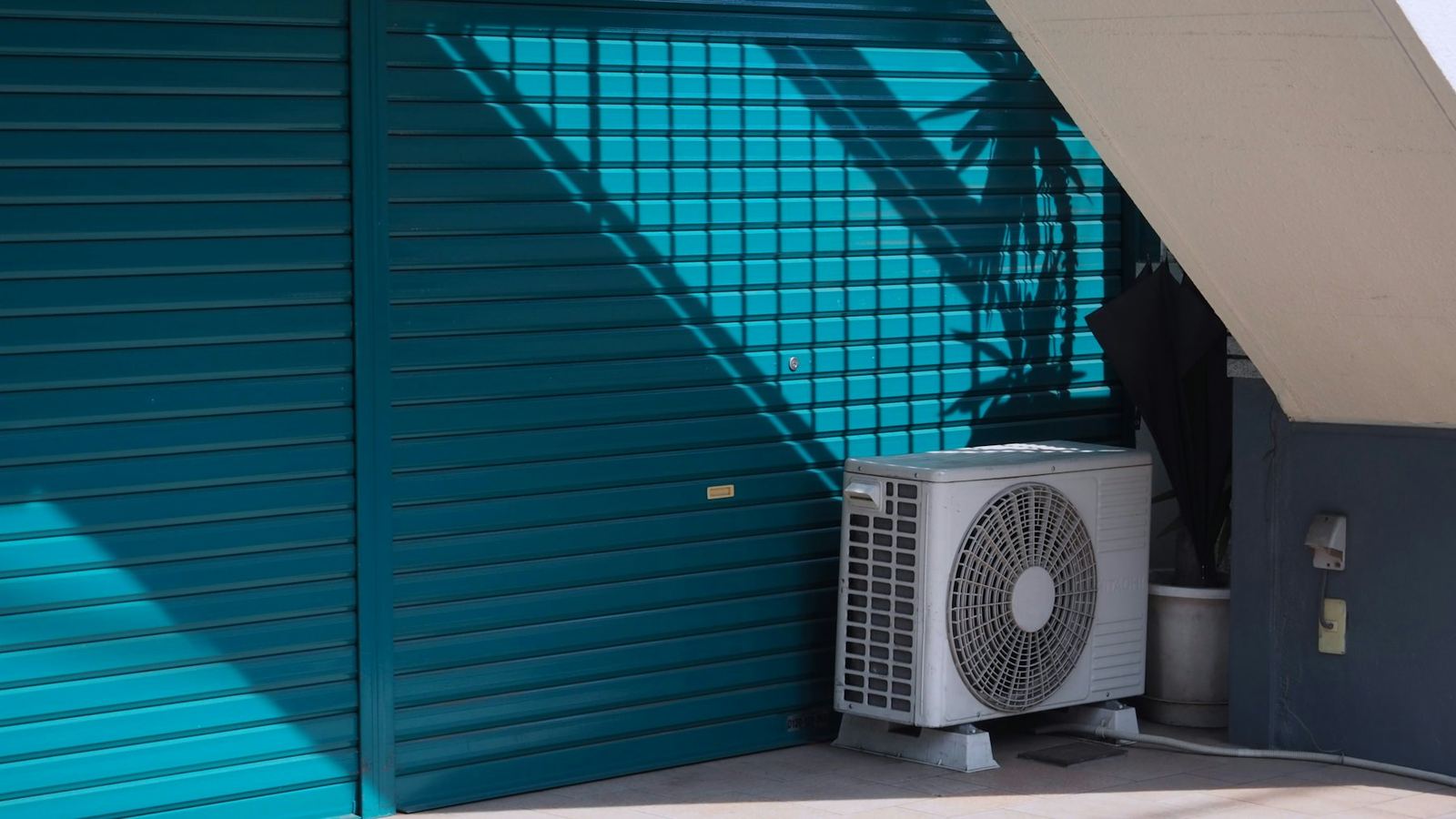 Air con outdoor unit on the ground next to a shop’s blue-green shutter