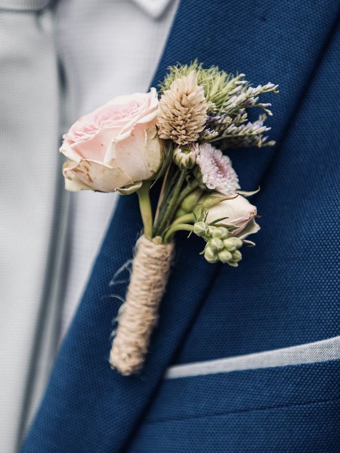Buttonhole of pink rose and sea holly, tied with jute, on the lapel of a blue suit