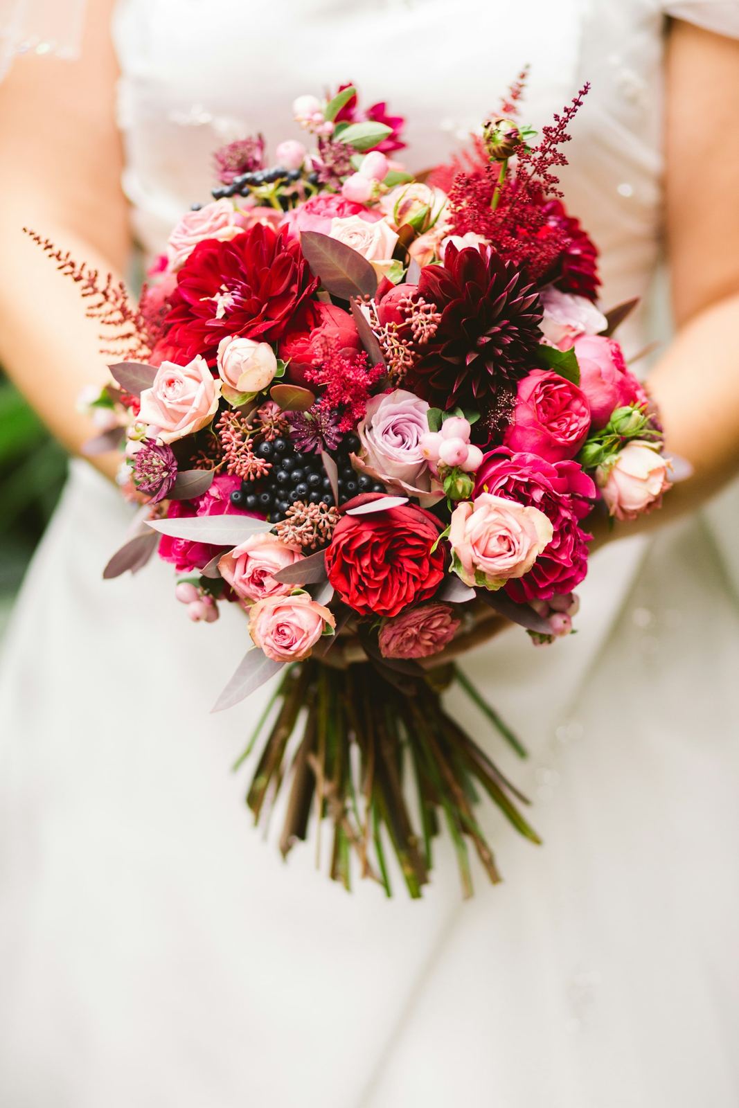 Bride holding a bouquet of roses and dahlias in reds and pinks