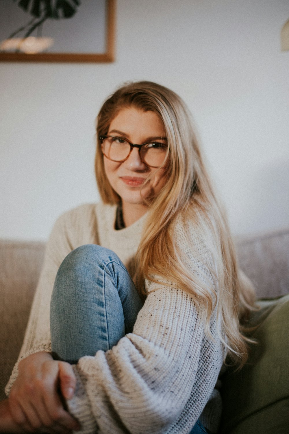 Sample portrait: a fair-haired woman with glasses sitting on a sofa and smiling
