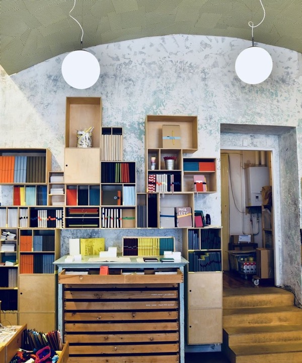 Wooden shelves with colourful notebooks and a chest of drawers under a vaulted ceiling