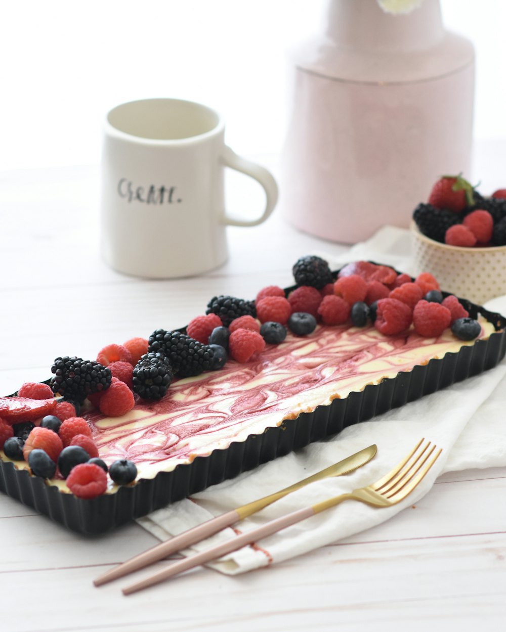 A rectangular cheesecake with red berries and pink swirls, in a black tin