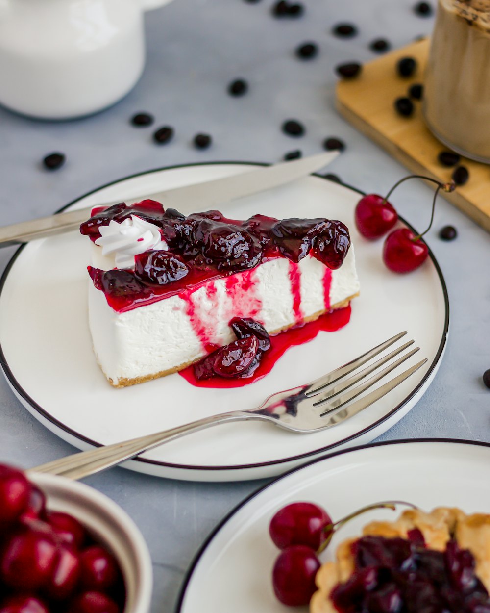 A slice of cheesecake with cherries in syrup, and fresh cherries around the plate