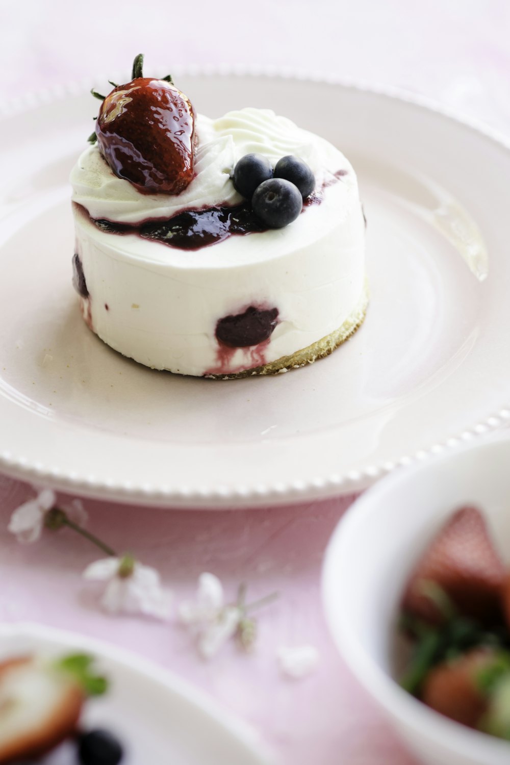 An individual cheesecake with blueberries and a strawberry on top, on a white plate
