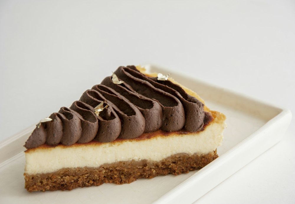 Porción de cheesecake con crema de chocolate por encima y base de galleta