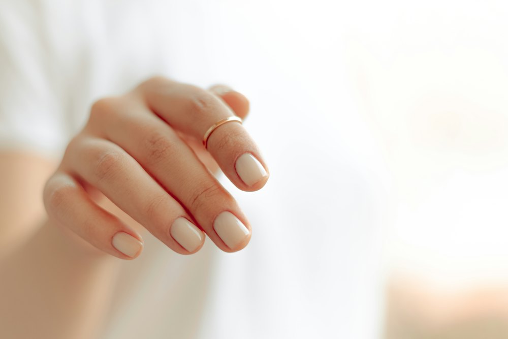 Mano con uñas cortas en tono nude y un anillo fino