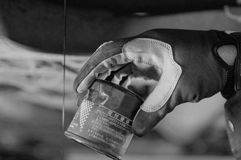 Gloved hand removing the oil filter as the old oil drains