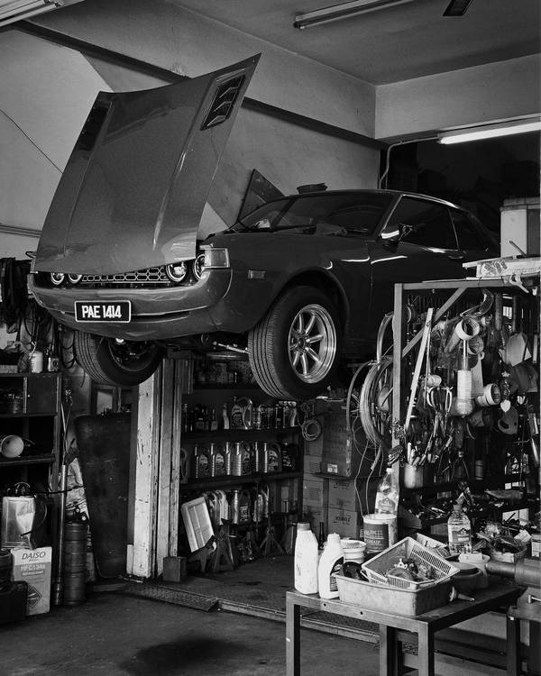 Classic car up on the lift with the bonnet open, between tool racks