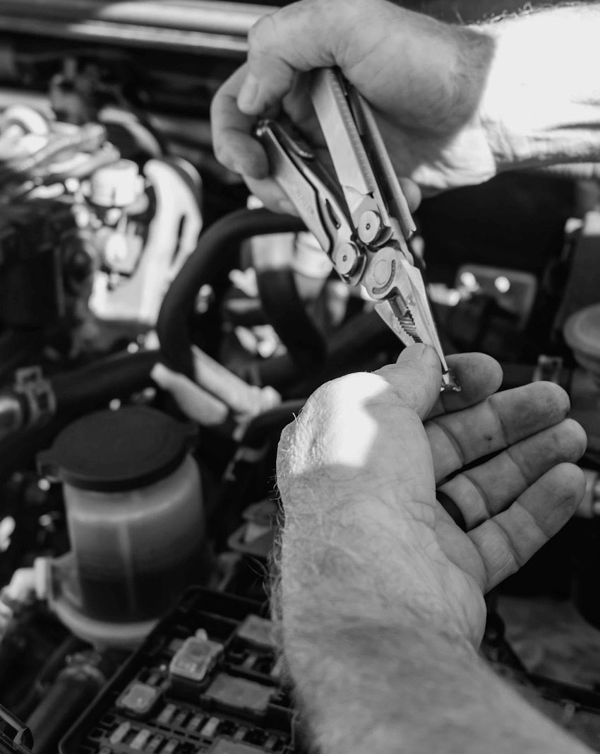 Hands pulling a fuse from the engine-bay fuse box with pliers